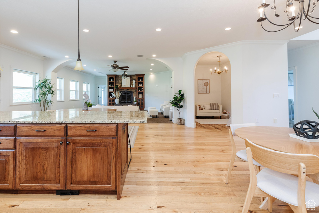 Kitchen with ceiling fan with notable chandelier, crown molding, light hardwood / wood-style flooring, and light stone counters