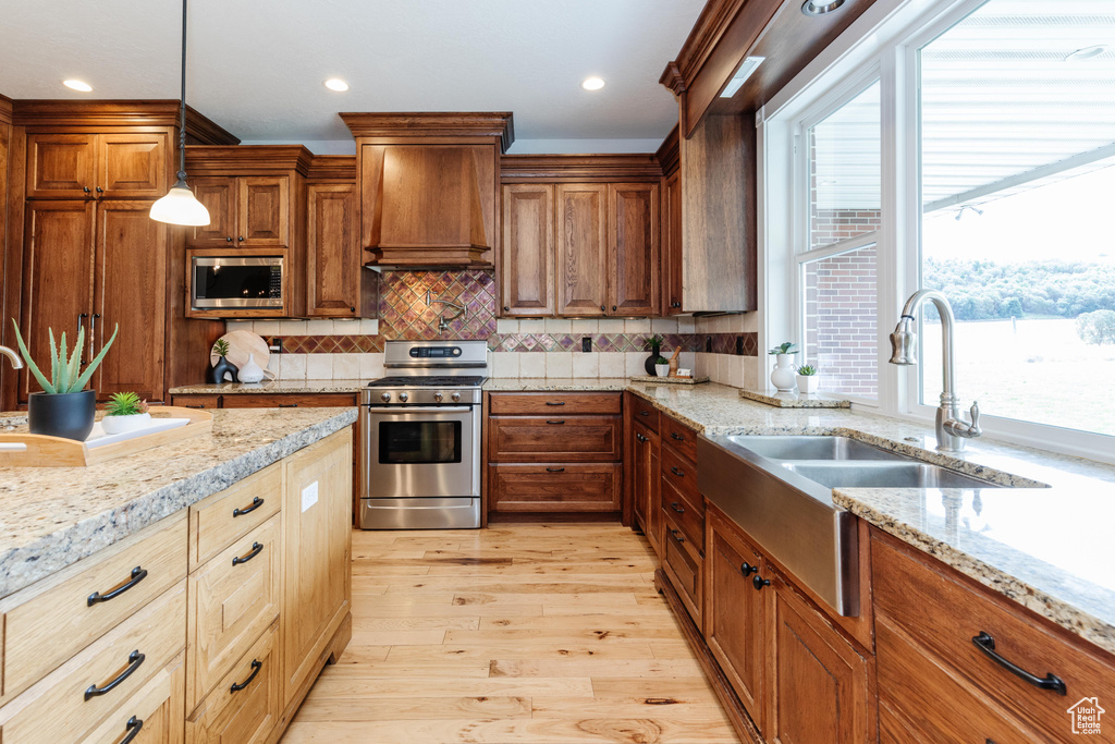 Kitchen featuring custom range hood, appliances with stainless steel finishes, light hardwood / wood-style flooring, tasteful backsplash, and pendant lighting