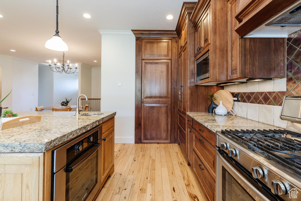 Kitchen featuring appliances with stainless steel finishes, custom exhaust hood, light hardwood / wood-style floors, tasteful backsplash, and hanging light fixtures