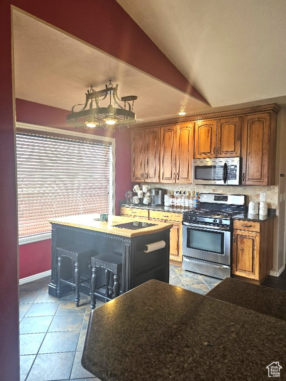 Kitchen featuring appliances with stainless steel finishes, a center island, lofted ceiling, and light tile patterned flooring