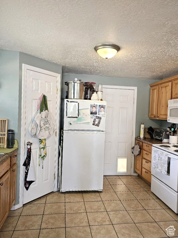 Kitchen with light tile patterned floors, a textured ceiling, and white appliances