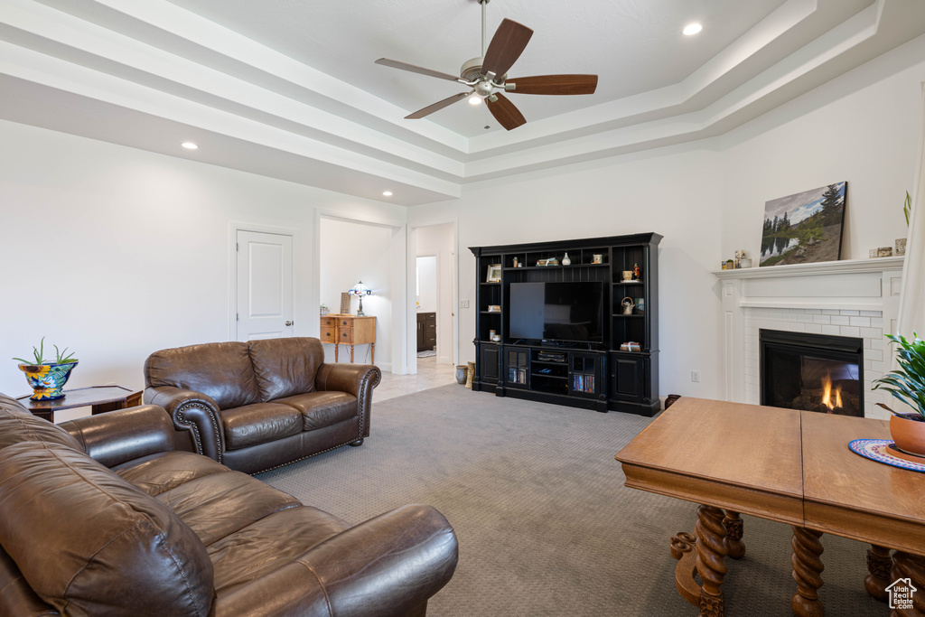 Carpeted living room with ceiling fan, a raised ceiling, a brick fireplace, and a high ceiling