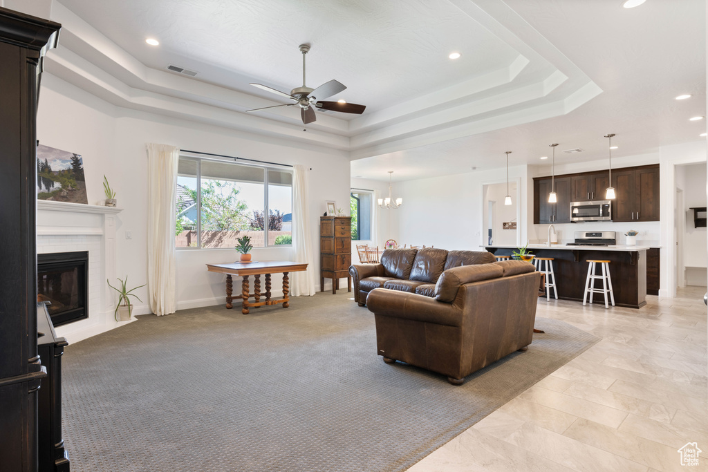 Living room featuring ceiling fan with notable chandelier, sink, light colored carpet, and a tray ceiling