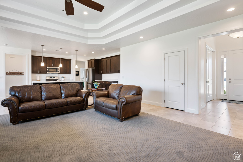 Living room with ceiling fan, light colored carpet, and a tray ceiling