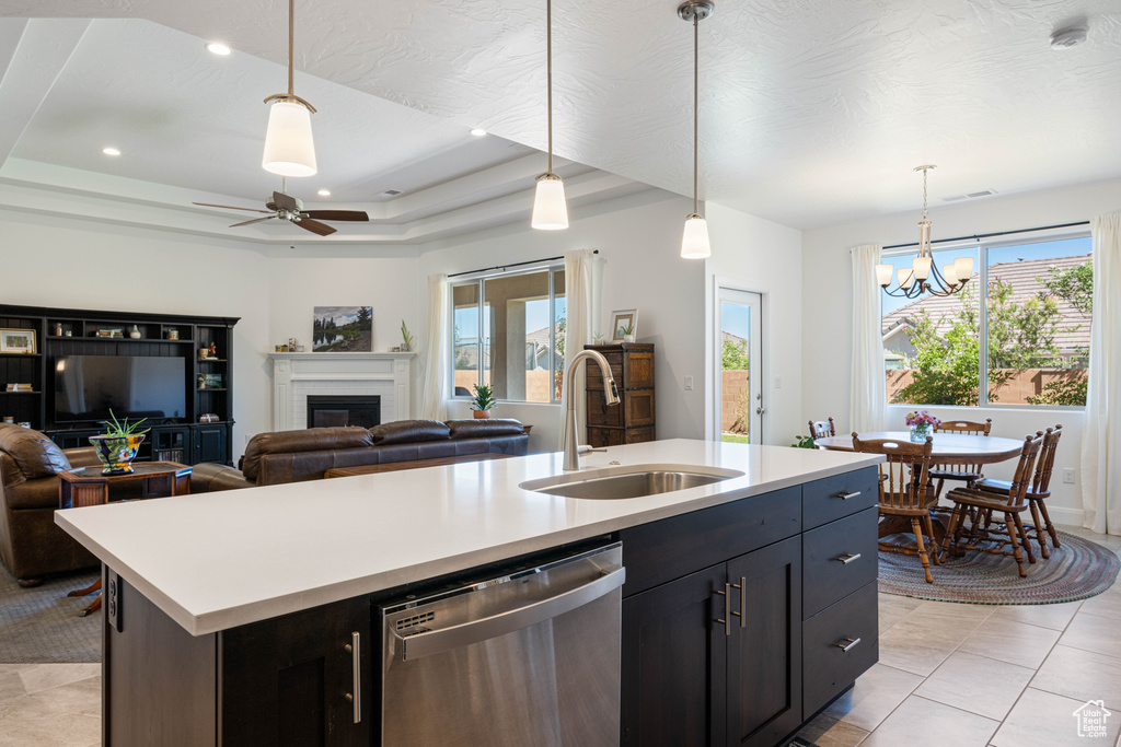 Kitchen featuring decorative light fixtures, stainless steel dishwasher, sink, a center island with sink, and a raised ceiling