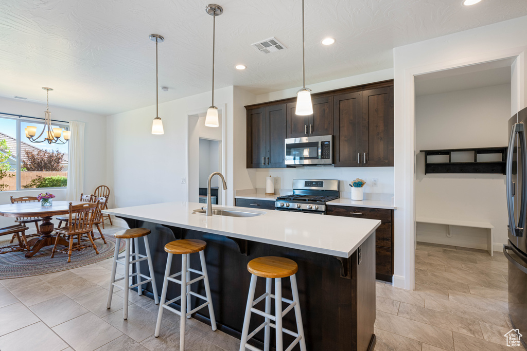 Kitchen featuring decorative light fixtures, sink, range, an island with sink, and a kitchen breakfast bar