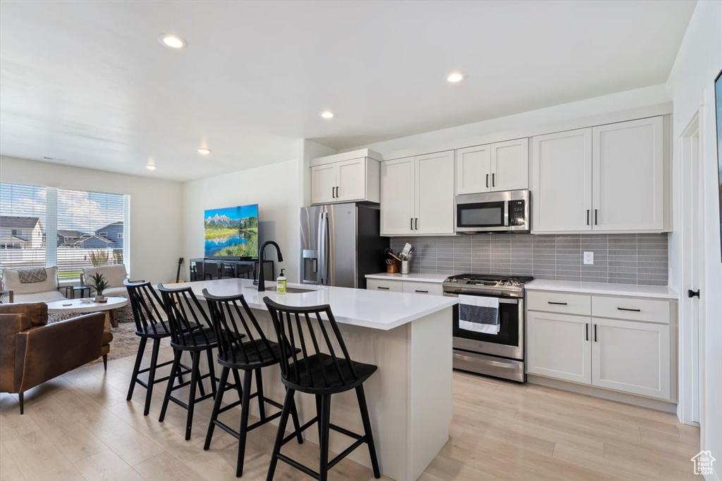 Kitchen featuring a center island with sink, light wood-type flooring, stainless steel appliances, backsplash, and sink