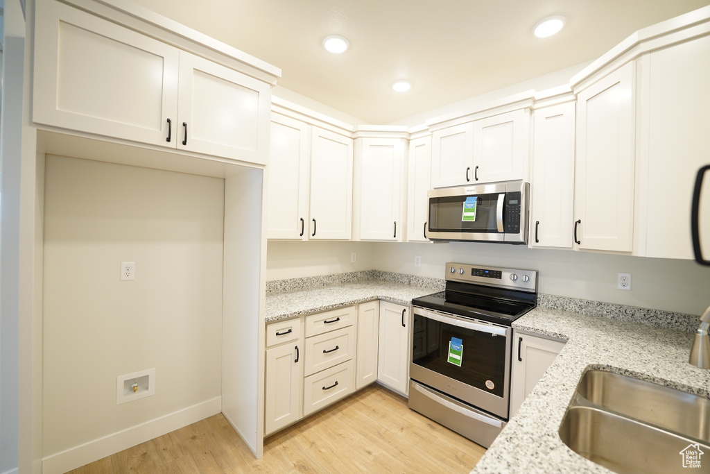 Kitchen featuring appliances with stainless steel finishes, light hardwood / wood-style flooring, and light stone counters