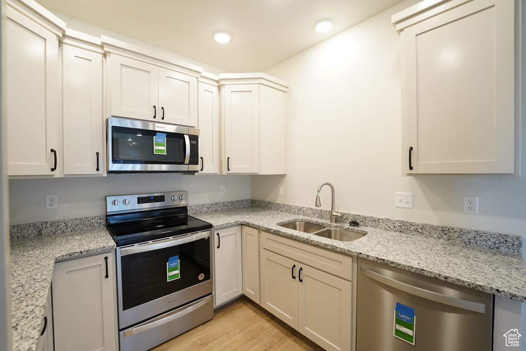 Kitchen featuring appliances with stainless steel finishes, white cabinetry, sink, light wood-type flooring, and light stone countertops