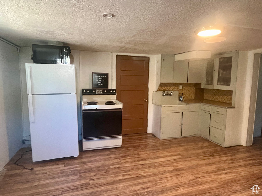 Kitchen featuring hardwood / wood-style floors, white appliances, a textured ceiling, sink, and decorative backsplash