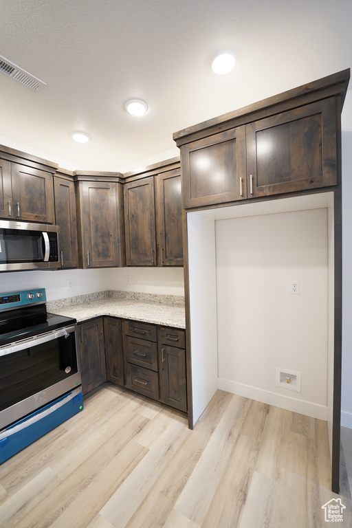 Kitchen with stainless steel appliances, light stone countertops, light wood-type flooring, and dark brown cabinetry