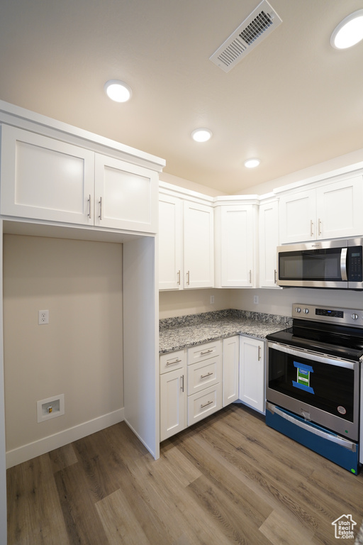 Kitchen with stainless steel appliances, light stone countertops, hardwood / wood-style floors, and white cabinets