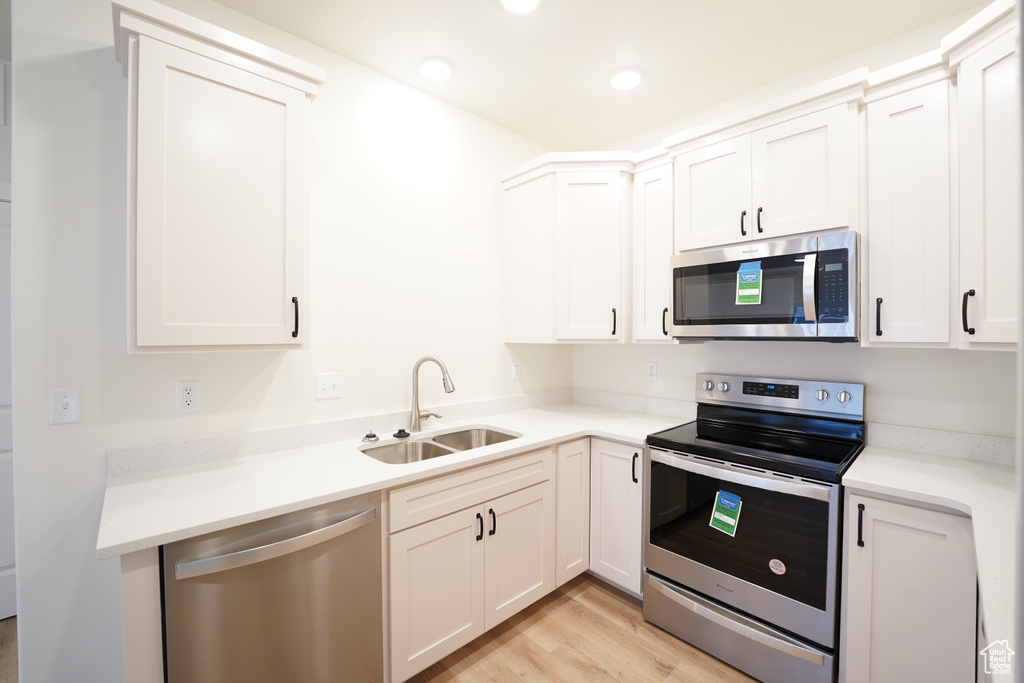 Kitchen with sink, stainless steel appliances, white cabinetry, and light wood-type flooring