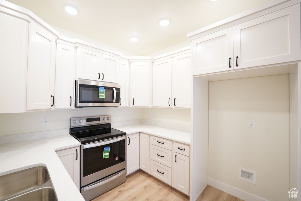 Kitchen featuring appliances with stainless steel finishes, light hardwood / wood-style flooring, and white cabinetry