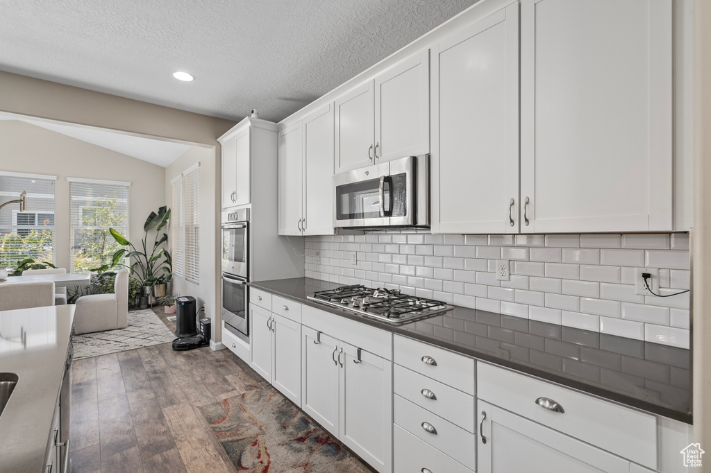 Kitchen featuring appliances with stainless steel finishes, white cabinetry, dark hardwood / wood-style floors, tasteful backsplash, and lofted ceiling