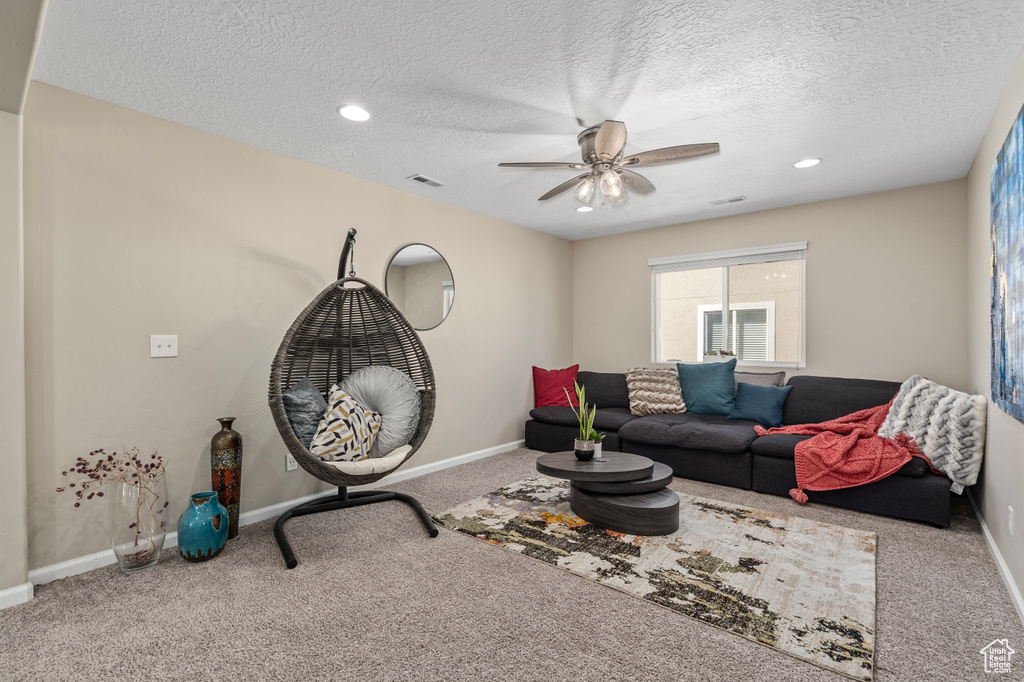 Carpeted living room with ceiling fan and a textured ceiling