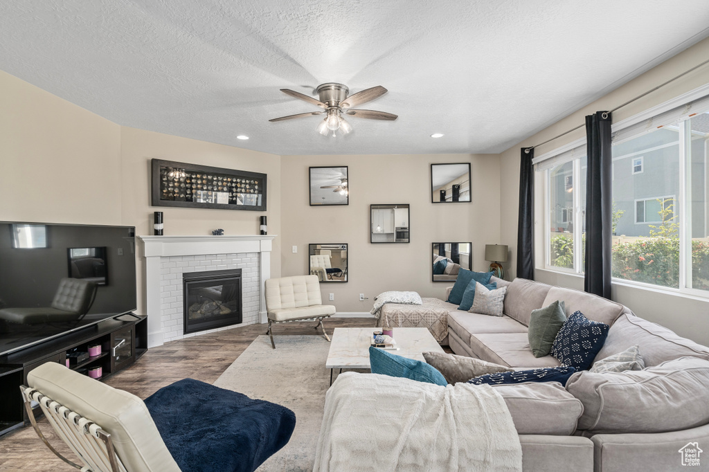 Living room with ceiling fan, a fireplace, a textured ceiling, and wood-type flooring