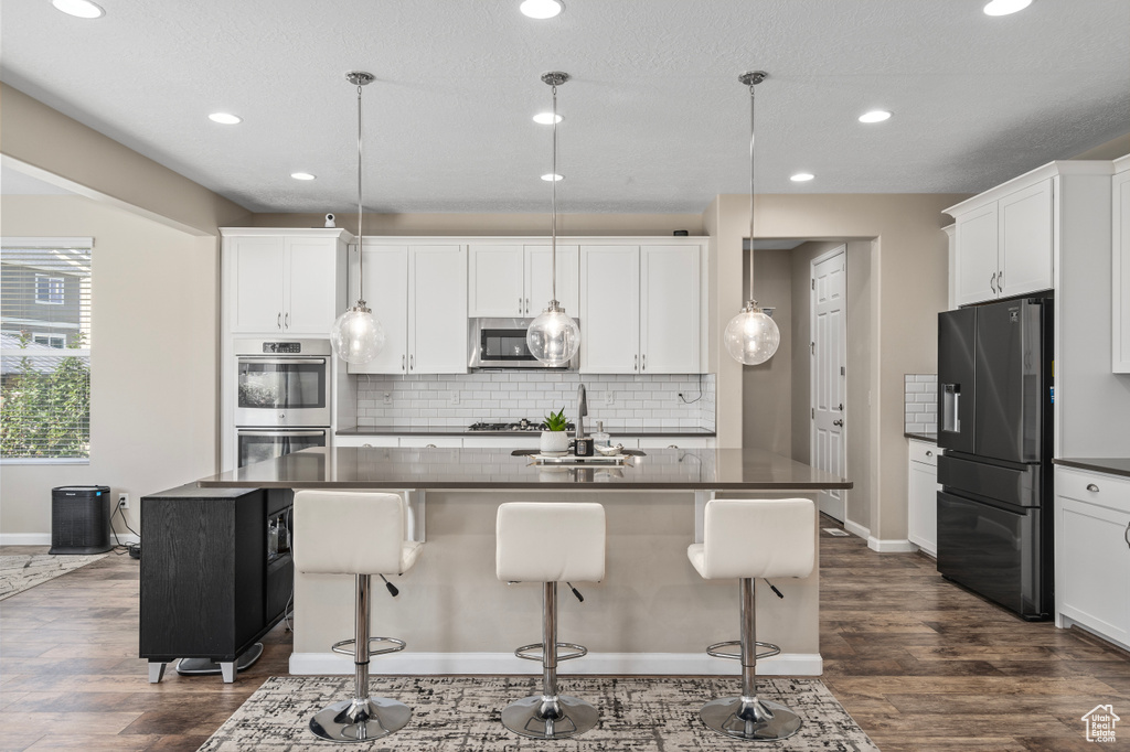 Kitchen with dark wood-type flooring, decorative backsplash, stainless steel appliances, a center island with sink, and white cabinets