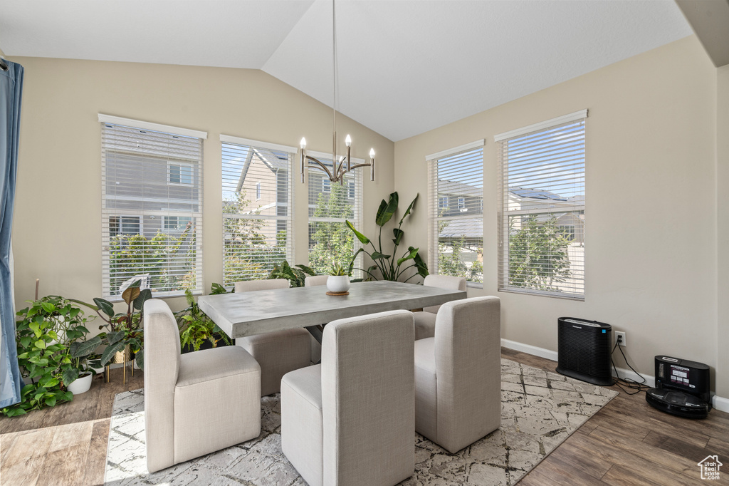 Dining area with light wood-type flooring, a wealth of natural light, vaulted ceiling, and an inviting chandelier