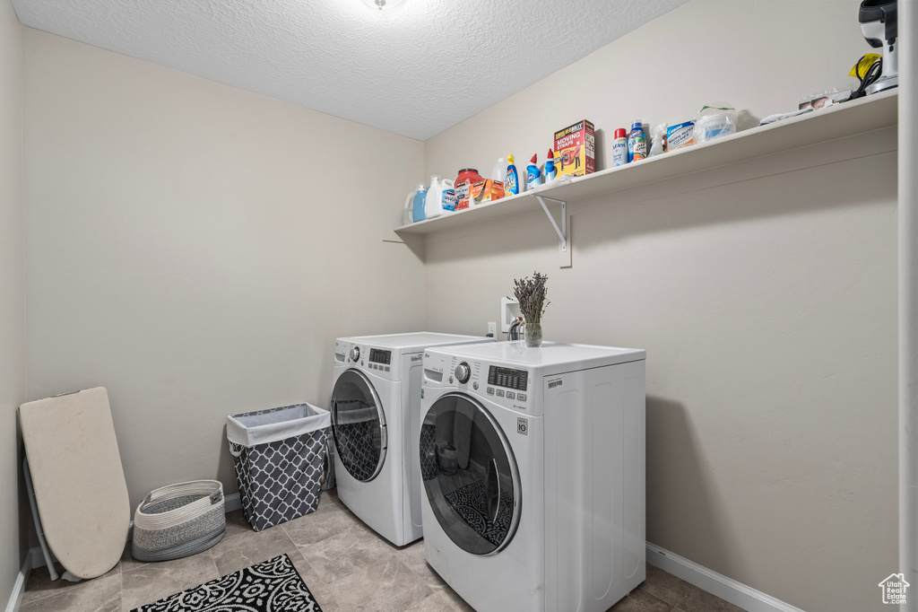 Laundry area with independent washer and dryer, a textured ceiling, and light tile patterned floors