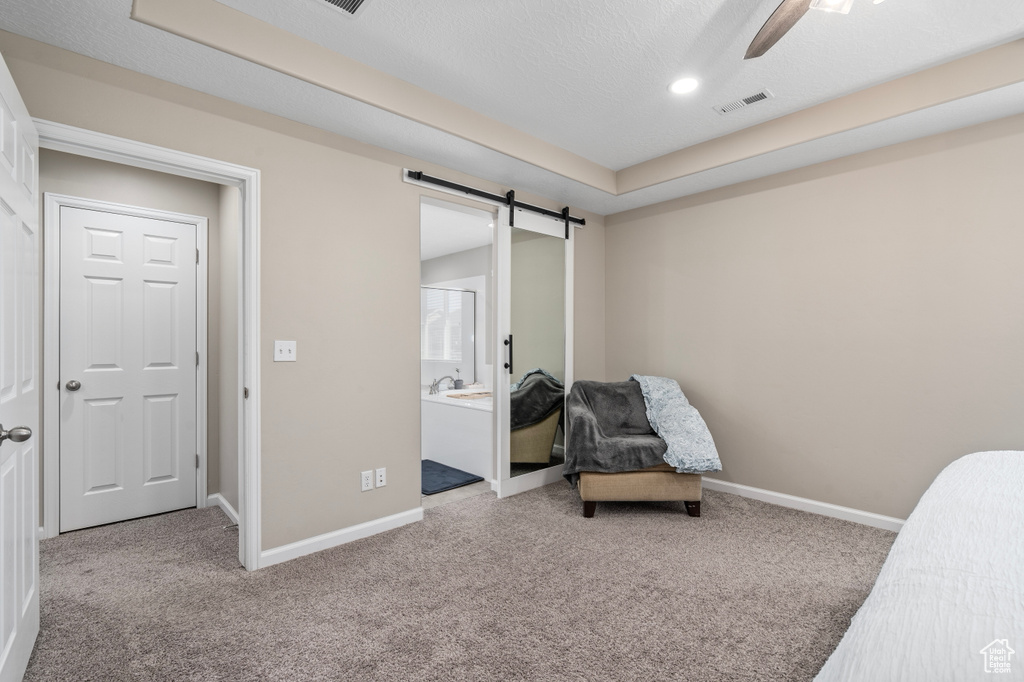 Carpeted bedroom featuring ceiling fan, a textured ceiling, ensuite bath, and a barn door