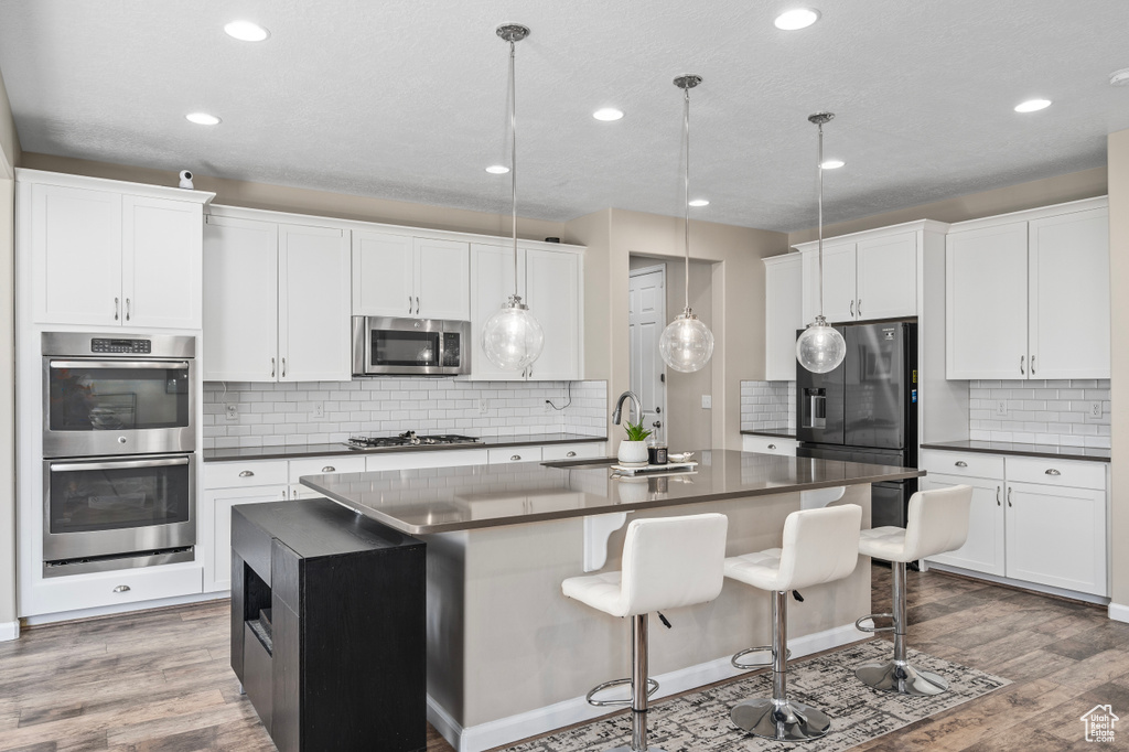 Kitchen featuring stainless steel appliances, a kitchen island with sink, decorative backsplash, and wood-type flooring