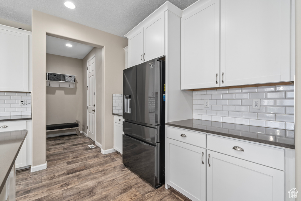 Kitchen featuring dark hardwood / wood-style floors, black fridge, tasteful backsplash, white cabinets, and a textured ceiling