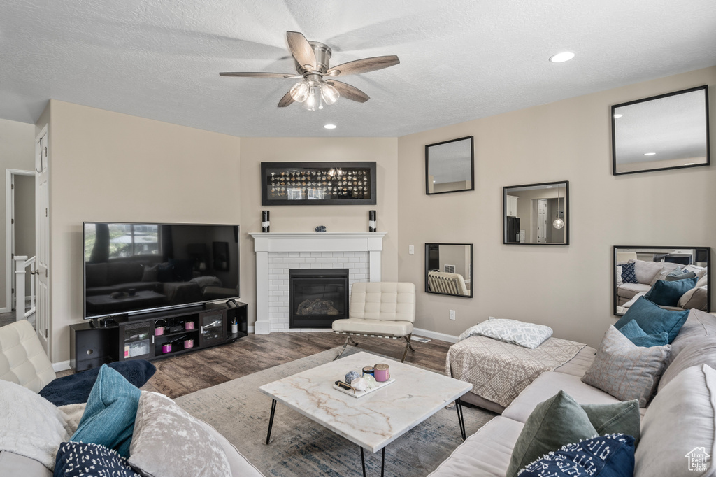 Living room featuring hardwood / wood-style flooring, a textured ceiling, a brick fireplace, and ceiling fan