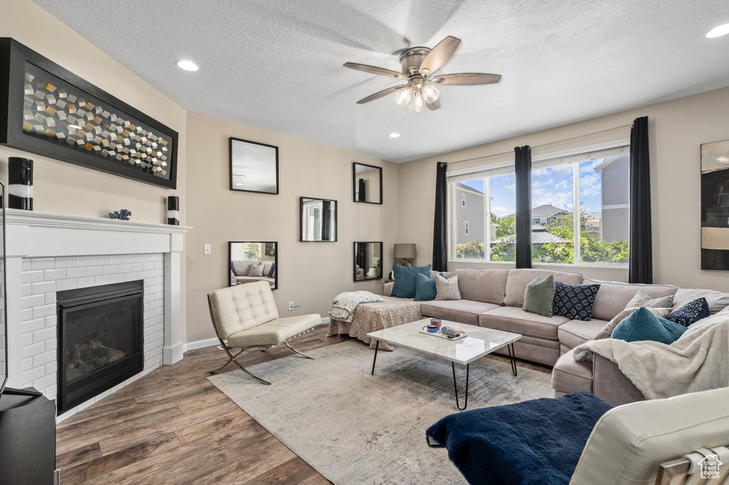 Living room featuring ceiling fan, a textured ceiling, a brick fireplace, and wood-type flooring