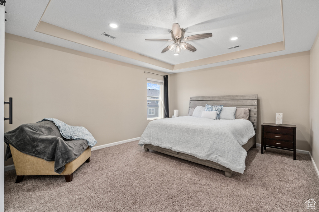 Bedroom with light colored carpet, a textured ceiling, a tray ceiling, and ceiling fan