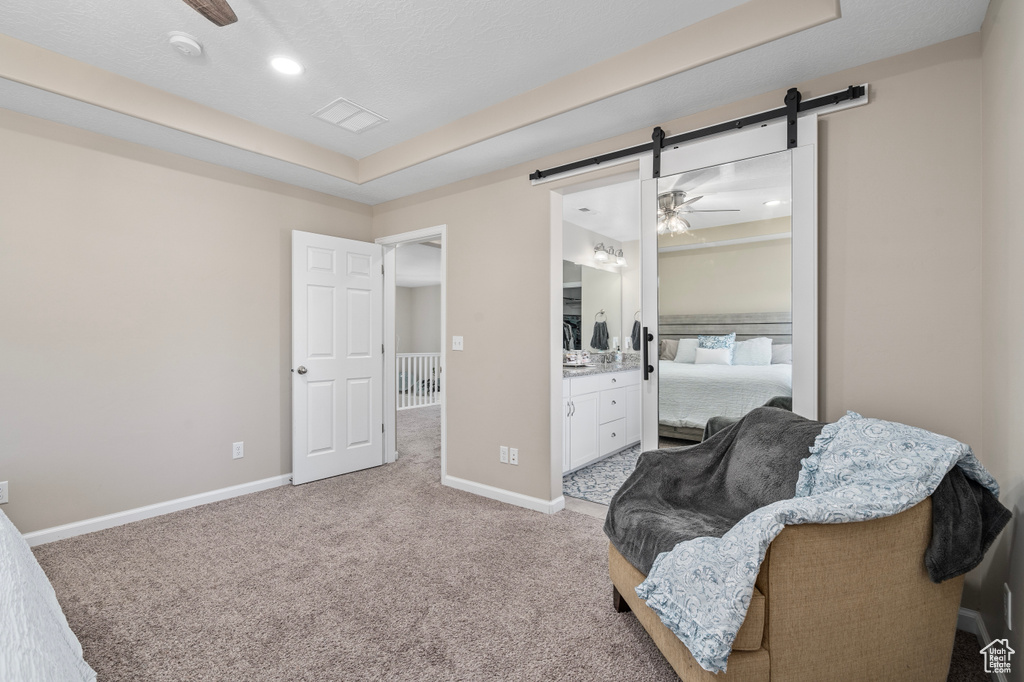 Living area with ceiling fan, light carpet, a raised ceiling, and a barn door