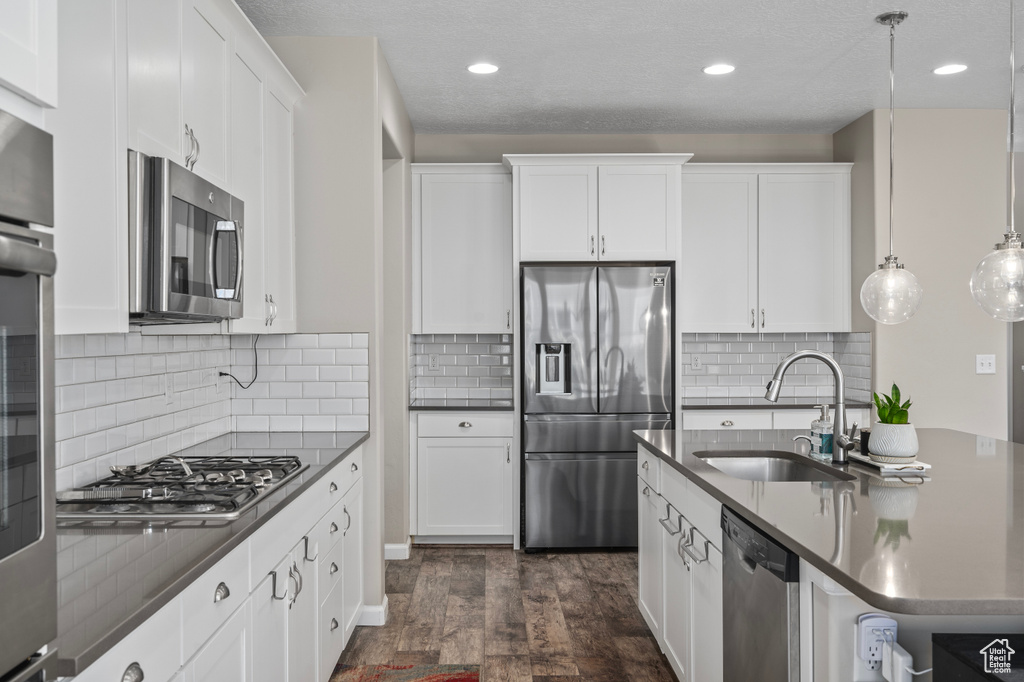 Kitchen featuring backsplash, dark hardwood / wood-style floors, pendant lighting, sink, and stainless steel appliances