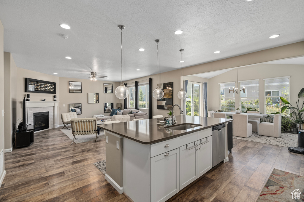 Kitchen featuring sink, a kitchen island with sink, ceiling fan with notable chandelier, dark hardwood / wood-style flooring, and a brick fireplace