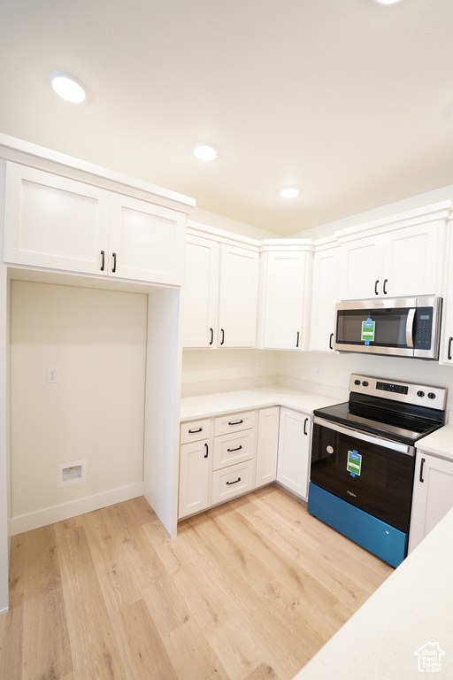 Kitchen with stainless steel appliances, white cabinetry, and light hardwood / wood-style flooring