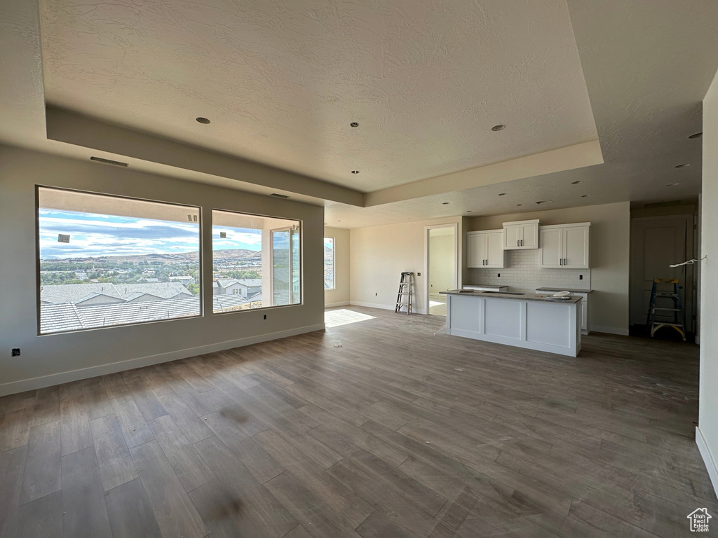 Unfurnished living room with a textured ceiling, wood-type flooring, and a raised ceiling