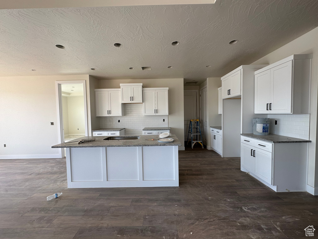 Kitchen featuring white cabinetry, decorative backsplash, and a center island with sink