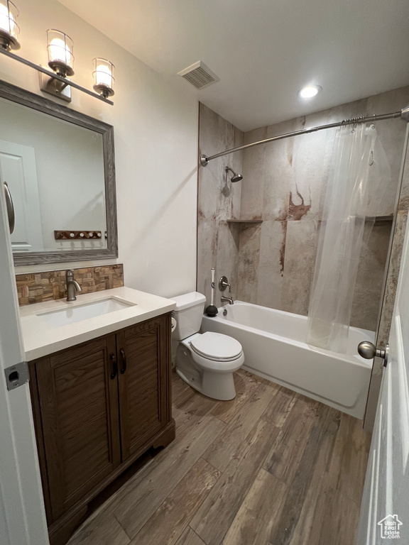 Full bathroom featuring backsplash, toilet, vanity, wood-type flooring, and shower / tub combo