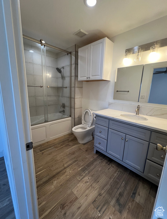 Full bathroom with enclosed tub / shower combo, vanity, wood-type flooring, and toilet