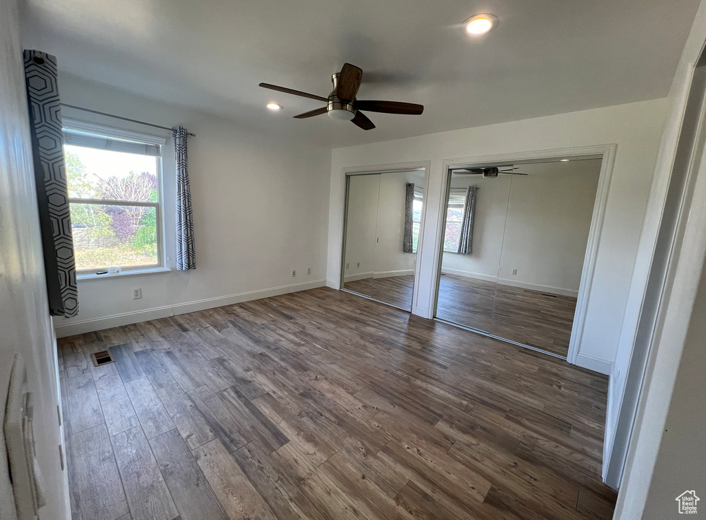 Unfurnished bedroom with ceiling fan, hardwood / wood-style flooring, and multiple closets