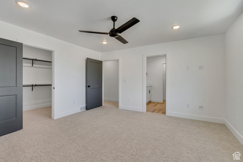 Unfurnished bedroom featuring light colored carpet, a closet, a walk in closet, and ceiling fan