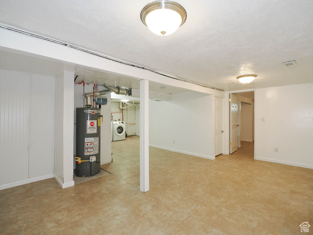 Basement with a textured ceiling, water heater, washer / dryer, and light tile patterned floors