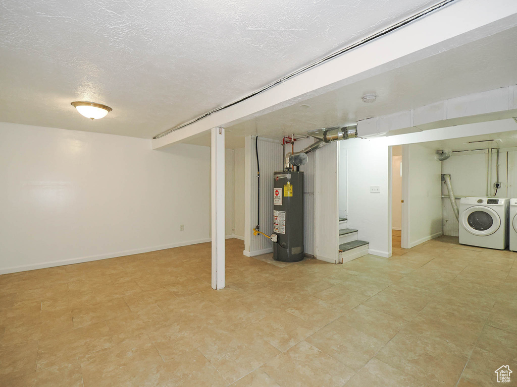 Basement featuring a textured ceiling, gas water heater, light tile patterned floors, and washing machine and dryer