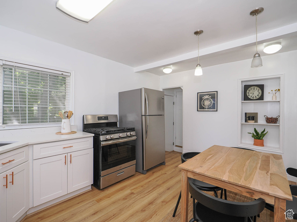 Kitchen featuring appliances with stainless steel finishes, white cabinetry, light wood-type flooring, and hanging light fixtures