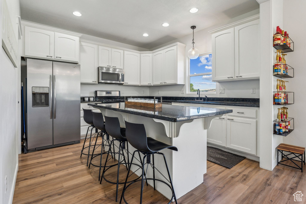 Kitchen with a center island, light hardwood / wood-style floors, white cabinetry, stainless steel appliances, and pendant lighting