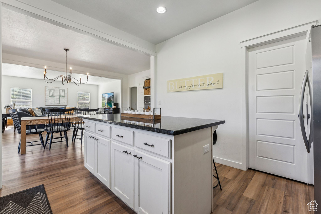 Kitchen featuring dark hardwood / wood-style floors, a kitchen breakfast bar, white cabinets, a kitchen island, and a notable chandelier