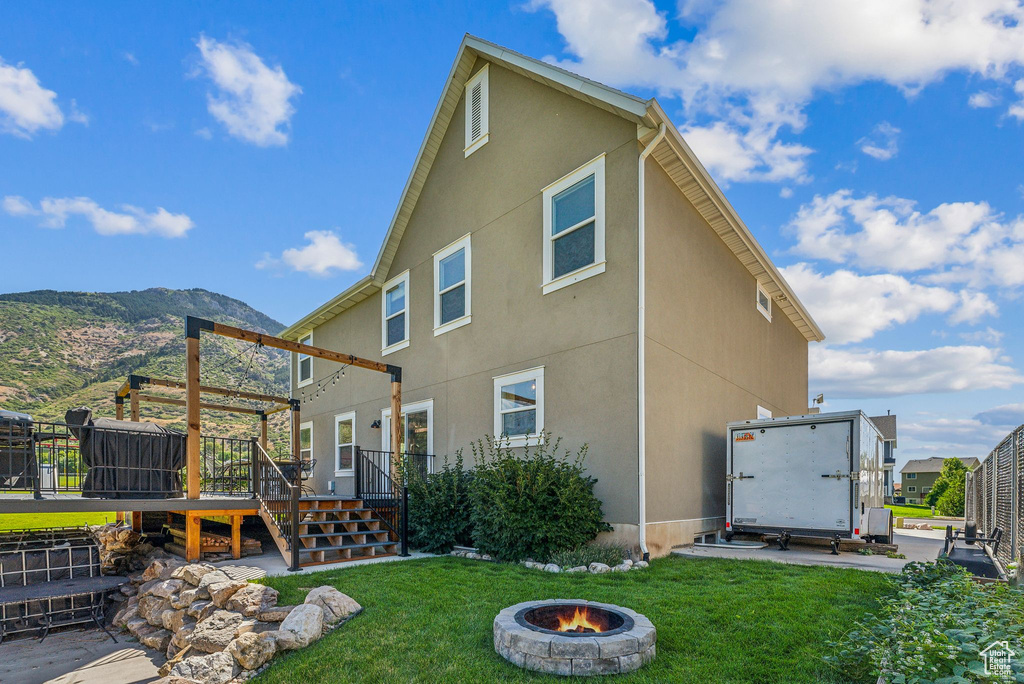 Rear view of house with a lawn, a deck with mountain view, and a fire pit