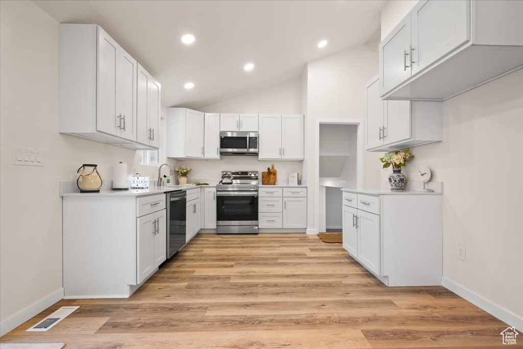 Kitchen with appliances with stainless steel finishes, light hardwood / wood-style flooring, and white cabinets