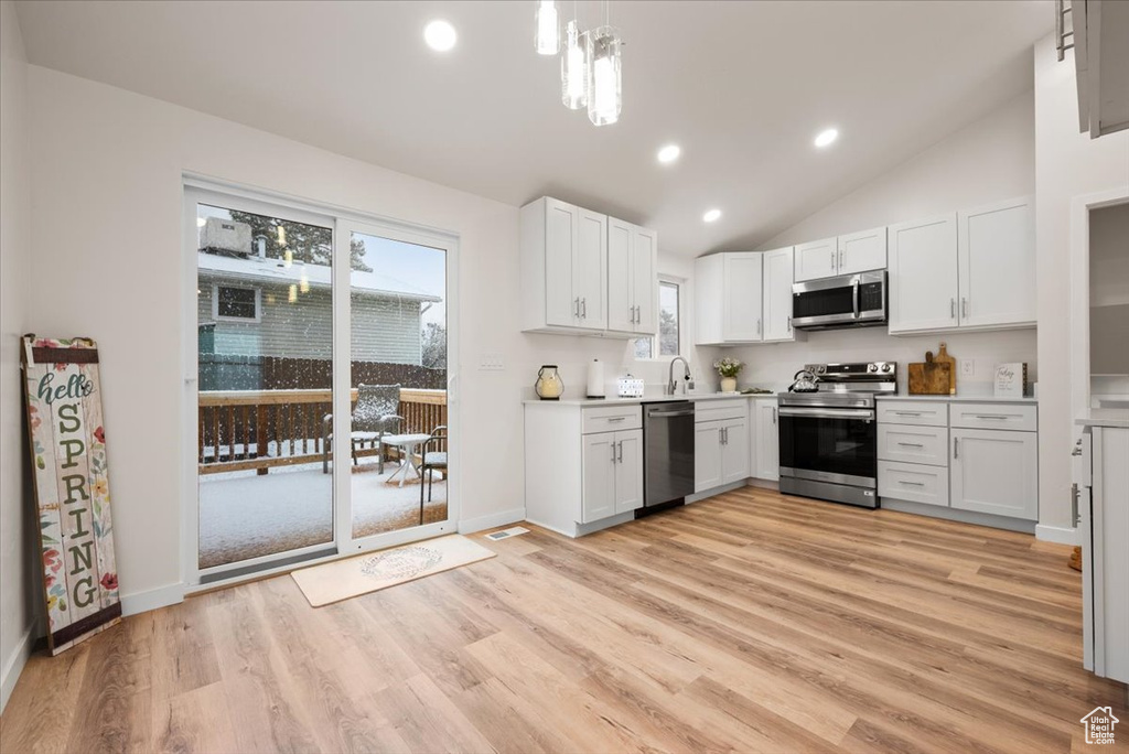 Kitchen featuring high vaulted ceiling, decorative light fixtures, light hardwood / wood-style flooring, stainless steel appliances, and white cabinets