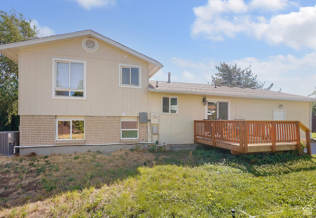 Back of house featuring a wooden deck, cooling unit, and a yard