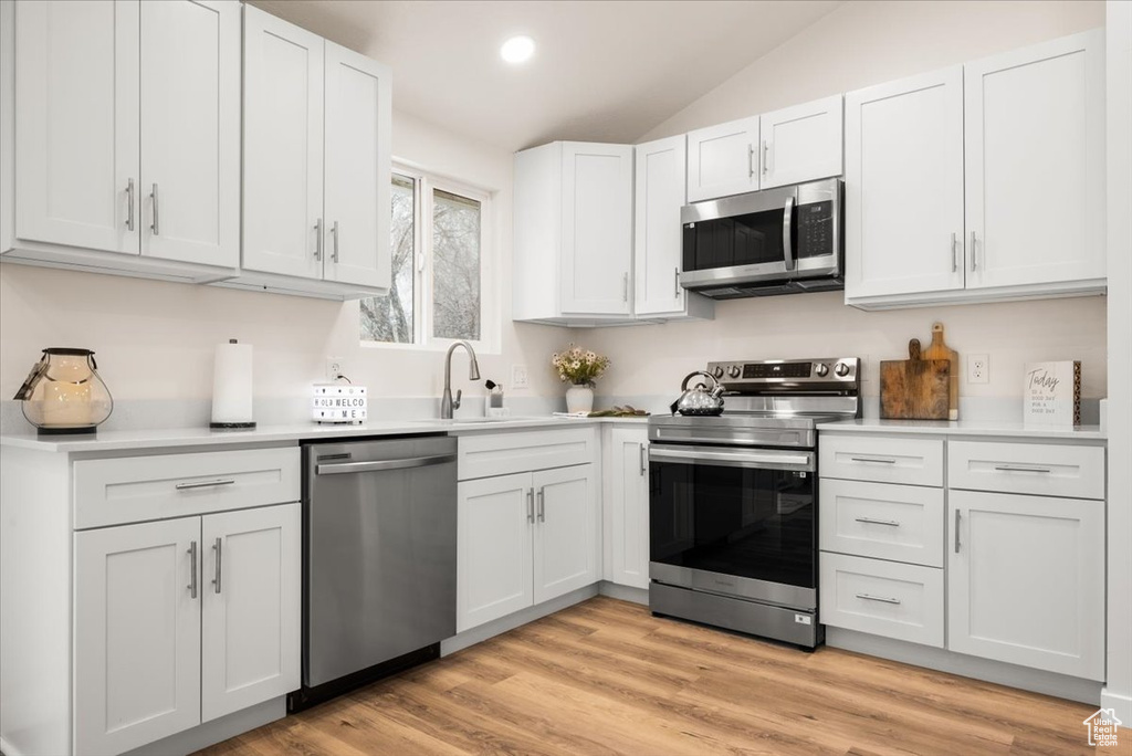 Kitchen with white cabinets, vaulted ceiling, light hardwood / wood-style flooring, and appliances with stainless steel finishes